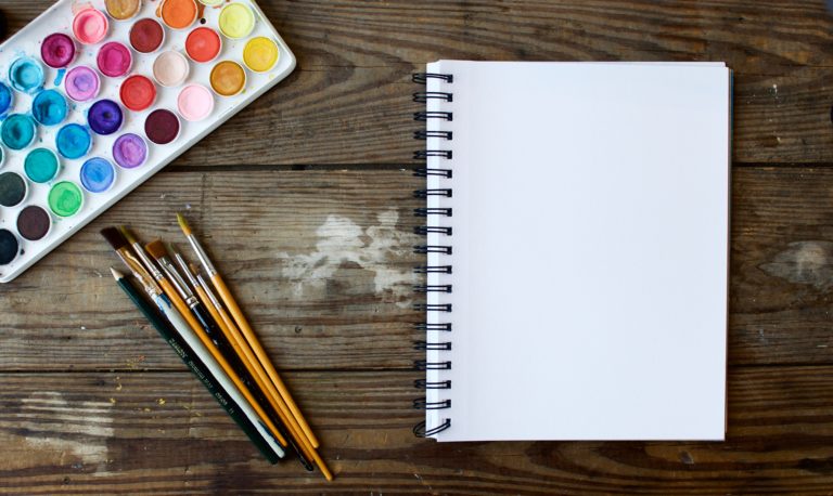 A set of multi-colored pains, paint brushes, and a drawing pad